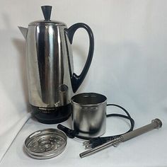 an electric coffee pot and other items on a white tablecloth with a black handle