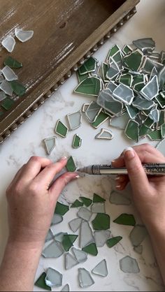 a woman is working on some green and white mosaic tiles with a marker in her hand