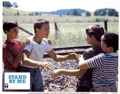 three boys are standing on the train tracks and one boy is holding something in his hand