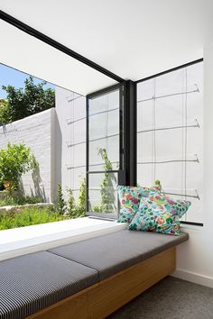 there is a bench with pillows on it in front of the glass wall and windows