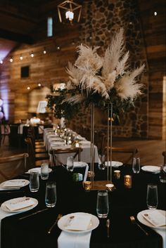 the table is set with white plates and silverware, black linens and tall centerpiece