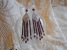 two pairs of earrings with red beads hanging from them on a lace doily next to a glass vase