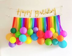 a happy birthday banner with balloons and streamers hanging from it's side in front of a white wall