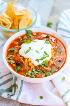 a bowl of chili with sour cream and tortilla chips next to it on a towel