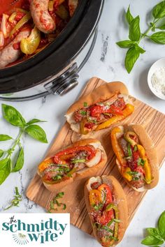 three hot dogs on buns with peppers and onions in the middle next to a slow cooker