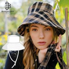 a woman wearing a hat and scarf in front of a tree with her hand on her chin