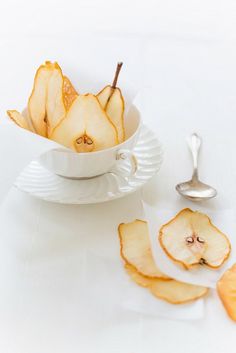 a bowl filled with sliced apples on top of a white table next to a spoon