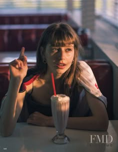 a woman sitting at a table with a milkshake in her hand and pointing to the side