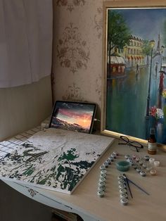 a laptop computer sitting on top of a desk next to a painting and other items