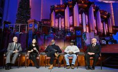 four people sitting on chairs in front of a pipe organ and christmas tree with lights