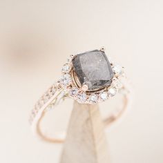 a fancy ring with a black diamond surrounded by white diamonds on a marble stand in front of a plain background