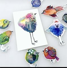 some colorful birds are sitting on top of a white surface and one is surrounded by cut outs