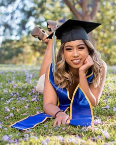 a woman in graduation cap and gown laying on the grass with her legs crossed, smiling at the camera