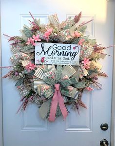 a wreath that says good morning with pink flowers and ribbons hanging on the front door