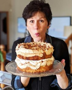 a woman holding a cake with frosting on it in front of her face and making a funny face