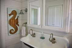 a bathroom sink with two mirrors and a seahorse painting on the wall above it