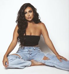 a woman sitting on the floor with her legs crossed wearing ripped jeans and a black crop top