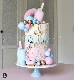 a pink and blue baby shower cake with balloons on it's top, sitting on a table