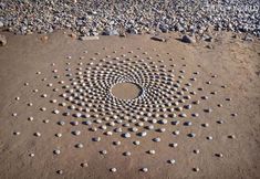 a circular design made out of rocks on the ground in front of some water and sand