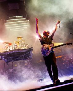 a man standing on top of a stage with his arms in the air and two guitars behind him