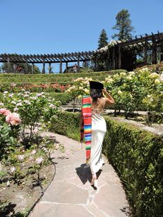 a woman walking down a path with a colorful blanket on her back and flowers in the background