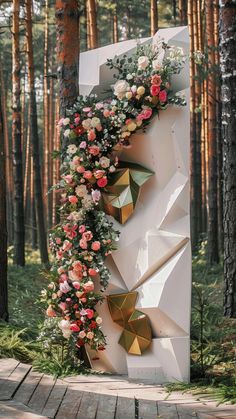 a white sculpture with flowers on it in the middle of a forest filled with trees