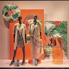 two mannequins in front of an orange and white wall with palm leaves