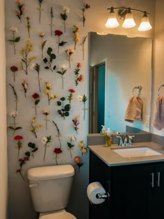 a white toilet sitting under a bathroom mirror next to a wall with flowers on it