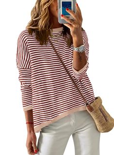 a woman taking a selfie with her cell phone while wearing white pants and a striped sweater