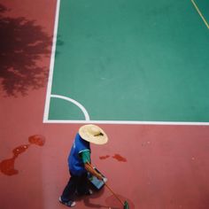 a man with a straw hat is sweeping the floor on a tennis court while holding a broom