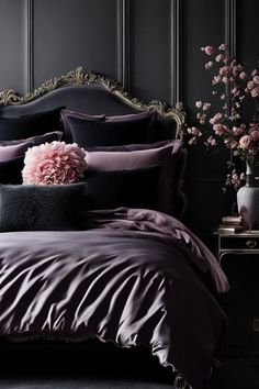 a bed with purple and black comforters in a dark room next to a flower vase