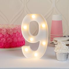 a lighted number 9 sits next to a cupcake on a cake stand with pink frosting