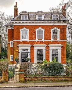 a red brick house with white trim and two story windows on the second floor is surrounded by greenery