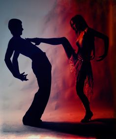 a man and woman dance in silhouette against a red background with the light from behind them