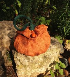 an orange knitted bag sitting on top of a rock in front of some bushes