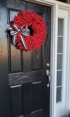 a black door with a red and white wreath hanging on it's front door