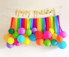 a happy birthday banner with balloons and streamers hanging from it's side in front of a white wall