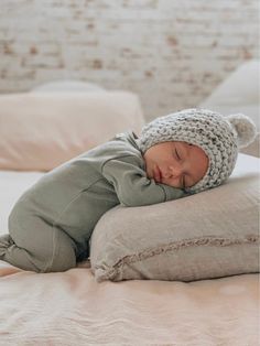 a baby sleeping on top of a pillow with a knitted bear hat over it's head