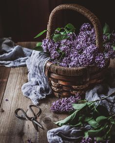 a basket filled with purple flowers sitting on top of a wooden table next to scissors