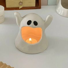 a white candle holder with a ghost face on it and a lit candle in the middle