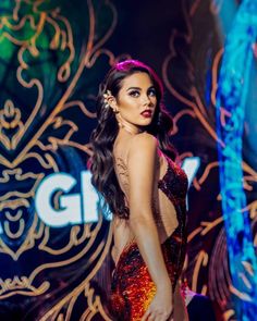 a woman in a red and gold dress is walking down the runway with her hand on her hip