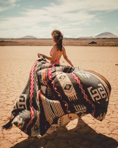 a woman sitting on top of a blanket in the desert