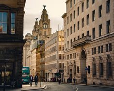 people are walking on the street in front of buildings with a clock tower behind them