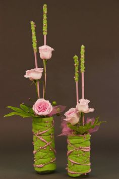 two green vases with pink roses and greenery in them on a gray background