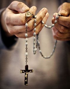 two hands holding a rosary with a cross hanging from it's end and the other hand