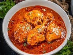 a white bowl filled with meat covered in sauce and garnished with parsley