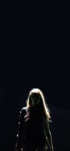 a woman with long hair and green makeup is standing in the dark, looking down