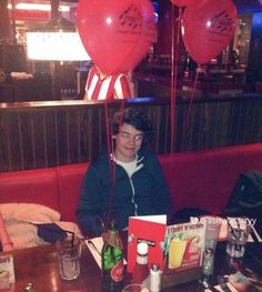 a man sitting at a table with two red balloons attached to the top of his head