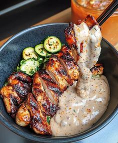 a bowl filled with meat and sauce next to cucumbers