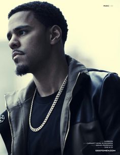 a man wearing a black shirt and jacket with a chain on his neck looking off to the side